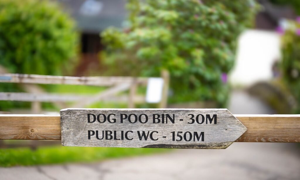 Wooden sign in UK indicating distance to dog poo bin and public WC.
